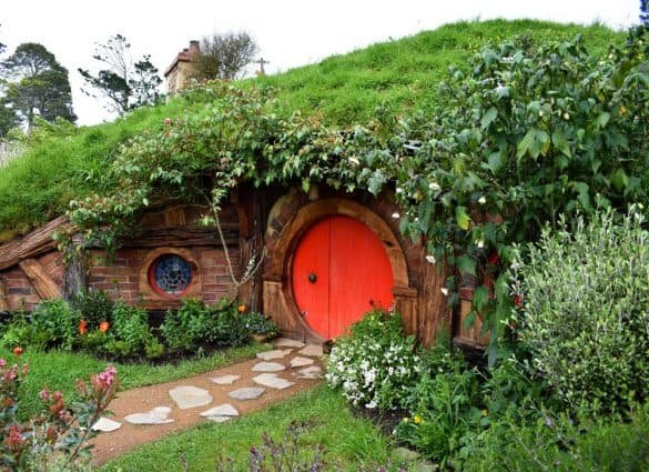 Hobbiton – New Zealand a red door at a hobbit house with a garden