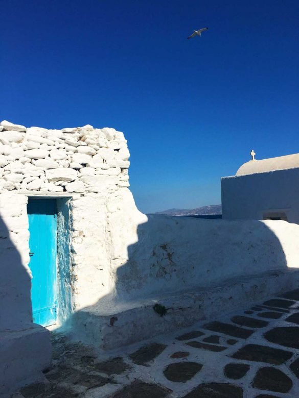white house with blue door at mykonos with a pebbled path