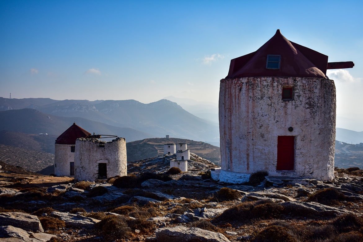seven traditional cycladic windmills with red roofs on rocky terrain
